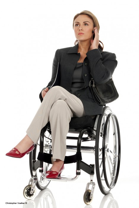 Young working woman who uses a wheelchair, holds folder and is on the phone.